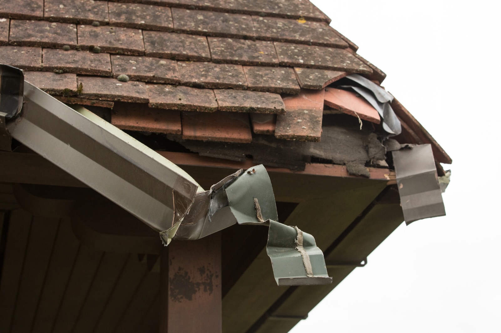 Beschadigde dakgoot en weggewaaide dakpannen door stormschade aan woning