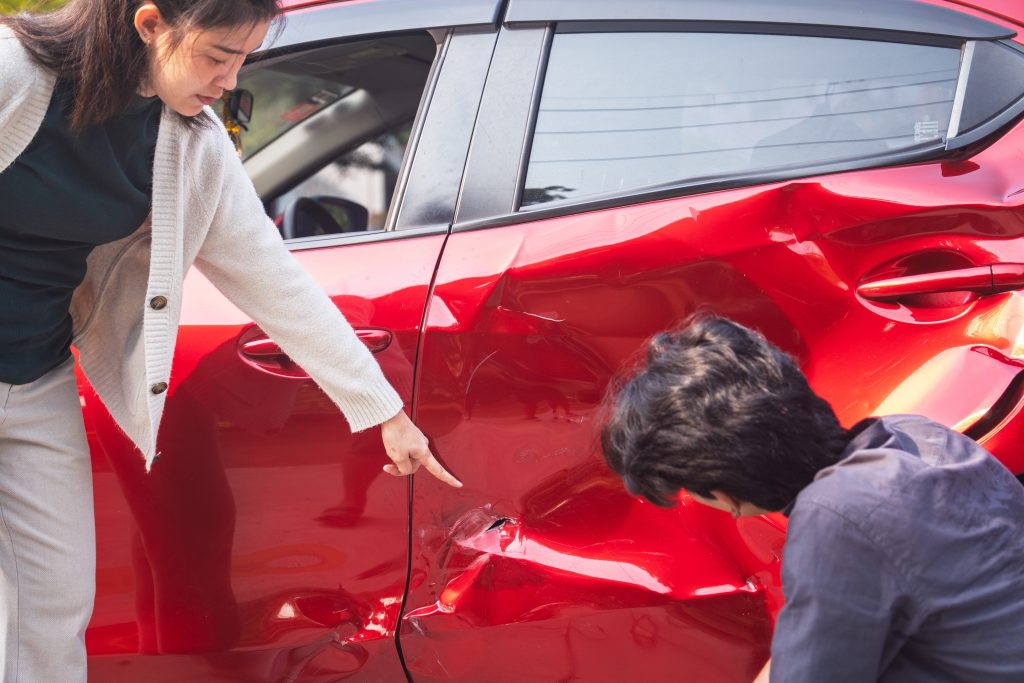 Vrouw wijst naar ernstige deuk in de rode autodeur terwijl een man de schade bekijk