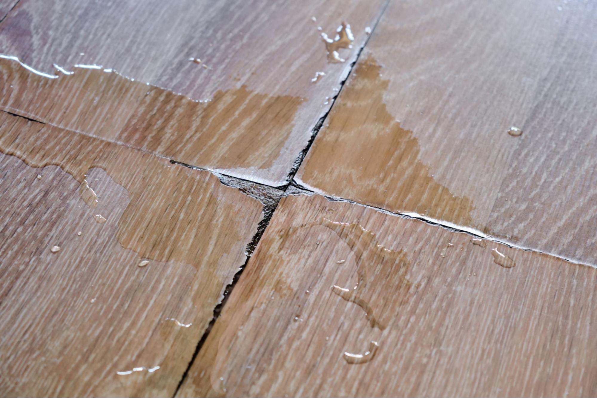 Waterschade door bovenburen zichtbaar op een houten vloer met opbollende naden