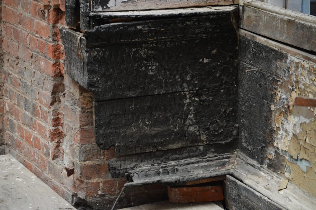 Verkoolde houten raamomlijsting met rook- en brandschade aan de gevel na een brand bij de buren