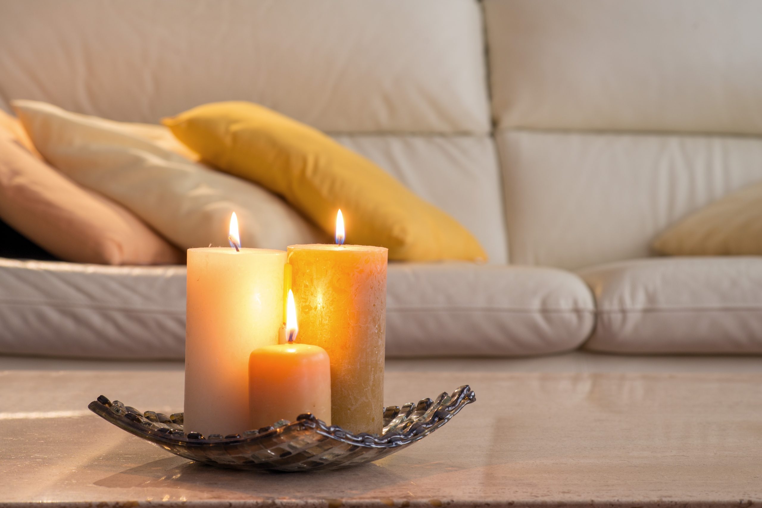 Brandende kaarsen in de woonkamer vlakbij een zetel en kussens.